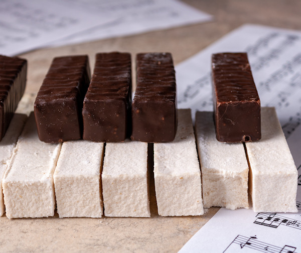 Piano keyboard made of white and chocolate marshmallow lies on music paper, selective focus